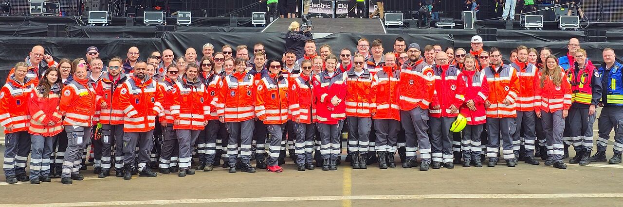 Gruppenfoto der DRK-Ortsvereine Adenau, Bad Breisig & Sinzig bei Rock am Ring. Das Team steht vor der Bühne.