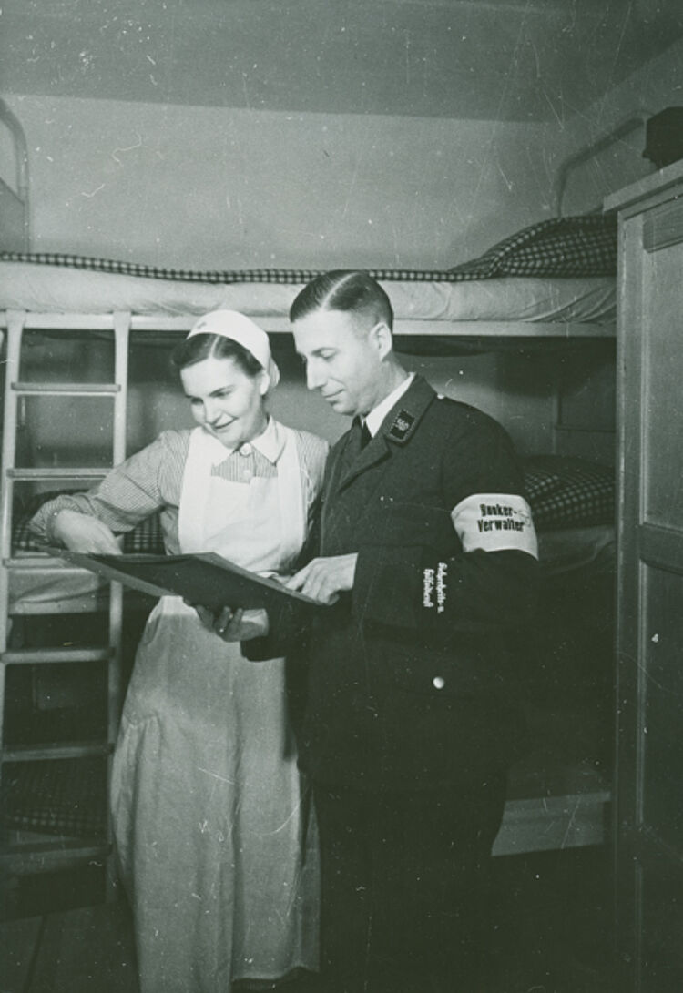 Eine DRK-Helferin und der Bunkerverwalter des Luftschutzbunkers in Berlin-Tempelhof prüfen die Liste mit den Namen der Anwesenden, 1941 (Stenner / DRK) Eine DRK-Helferin und der Bunkerverwalter des Luftschutzbunkers in Berlin-Tempelhof prüfen die Liste mit den Namen der Anwesenden, 1941 (Stenner / DRK)