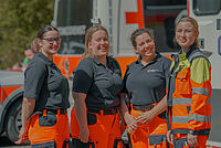 Vier Frauen, die im Rettungsdienst tätig sind, stehen lachend vor einem Rettungswagen.